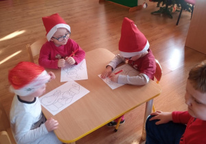 Dzieci kolorują kredkami sylwetę Mikołaja.